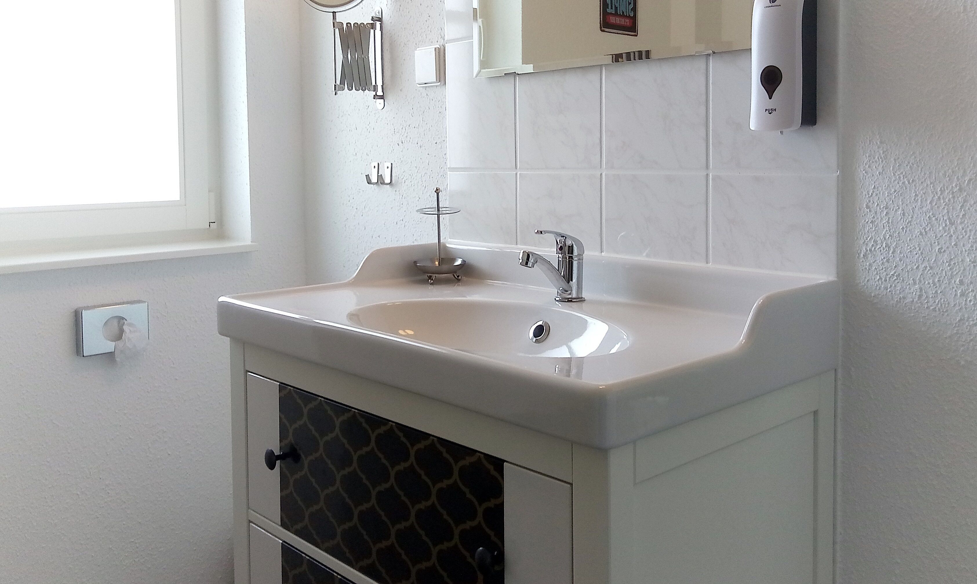 A bathroom with a white sink, a mirror, and a towel dispenser.