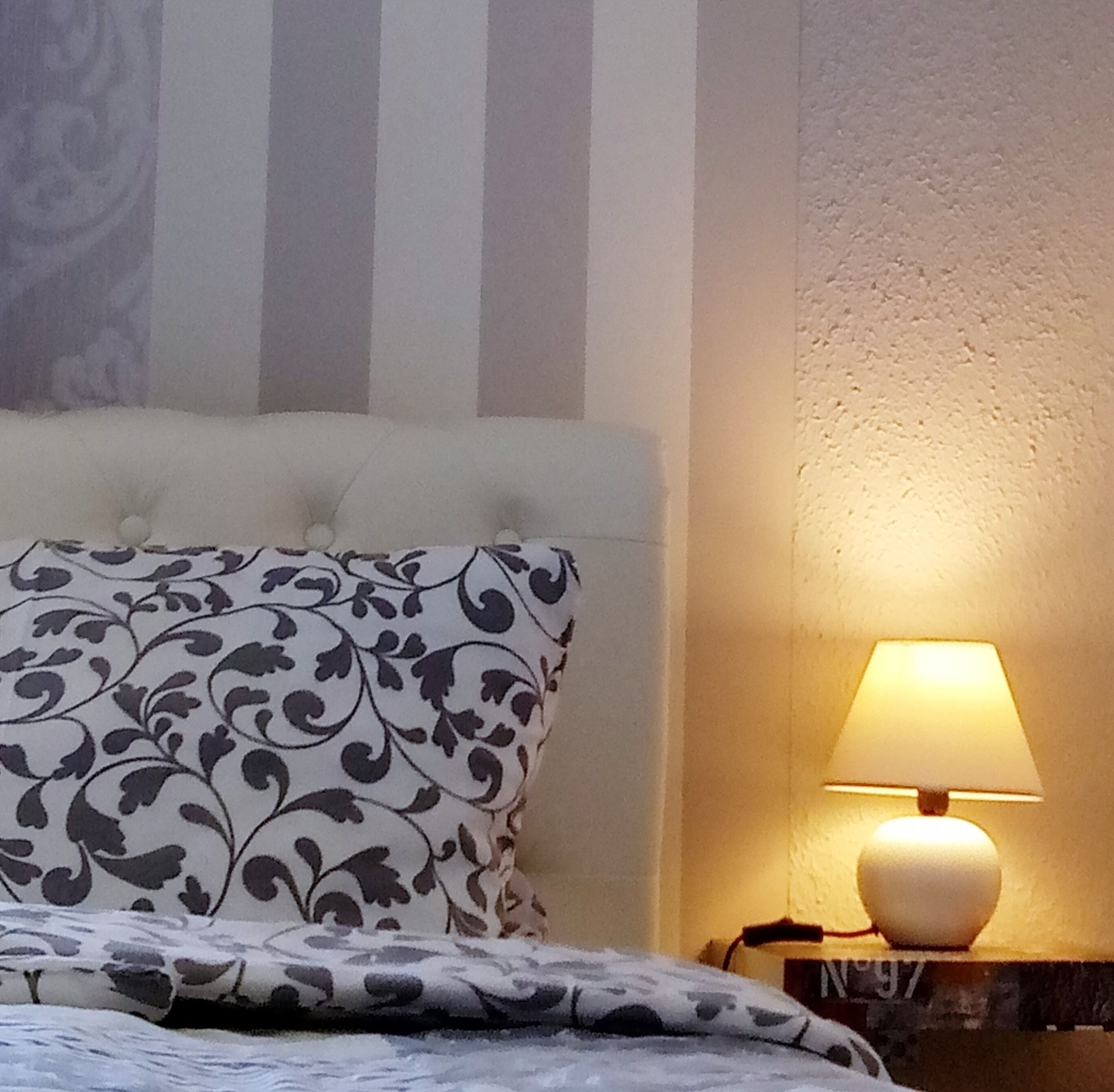 Ein Bett mit gemusterten Kissen, einer Nachttischlampe und einer gestreiften Wand.