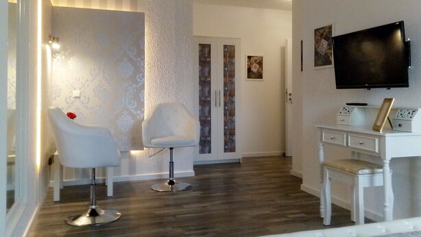 A modern living room with a wooden floor, a white sofa, a white armchair, a TV mounted on the wall, and a small white cabinet. - Villa Regina (Moehnesee)