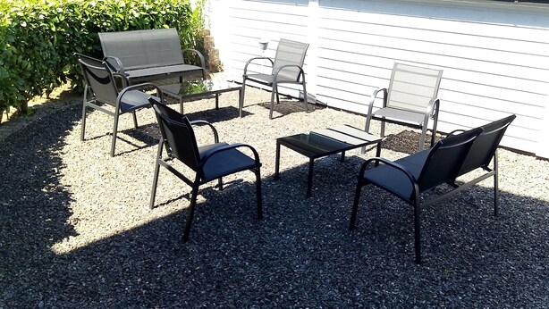 Un espacio al aire libre con cuatro sillas y una mesa, rodeado de grava y un seto.