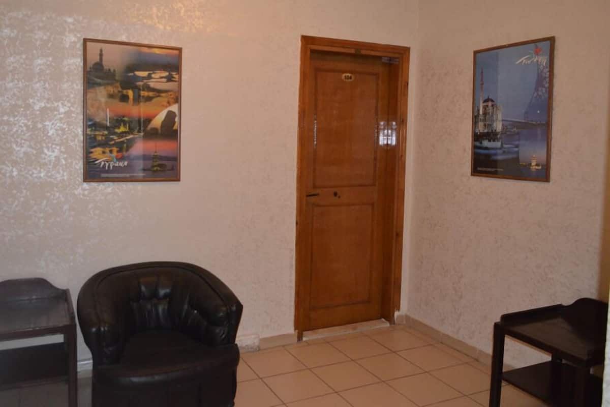 A room with a wooden door, two framed pictures on the wall, a black leather chair, and a small table.