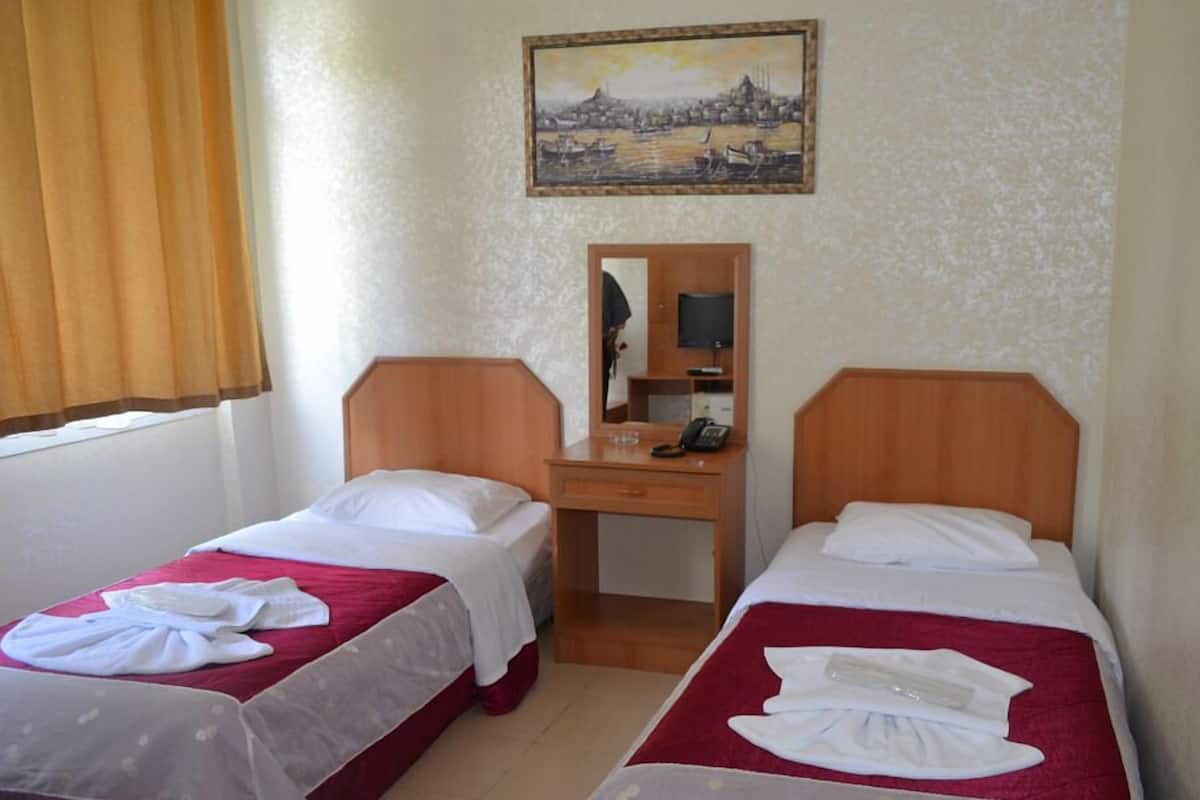 A hotel room with two single beds, a desk with a mirror, and a painting on the wall.
