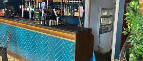 A bar area with a reception desk, shelves of bottles, and a patterned floor.