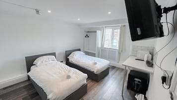 A bedroom with two beds, a small desk, a radiator, and a television mounted on the wall.