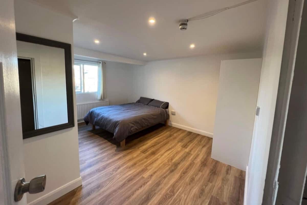 Un dormitorio con cama, suelo de madera, una ventana y una puerta.