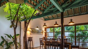 A dining area with wooden furniture and pendant lighting, a large window with a view of greenery, and a ceiling with a green lattice design. - Green Casa (Galle)