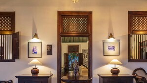 A hallway with two side tables, each with a lamp and a framed picture. A central table with a decorative backrest is flanked by a wooden door with a lattice design. - Green Casa (Galle)