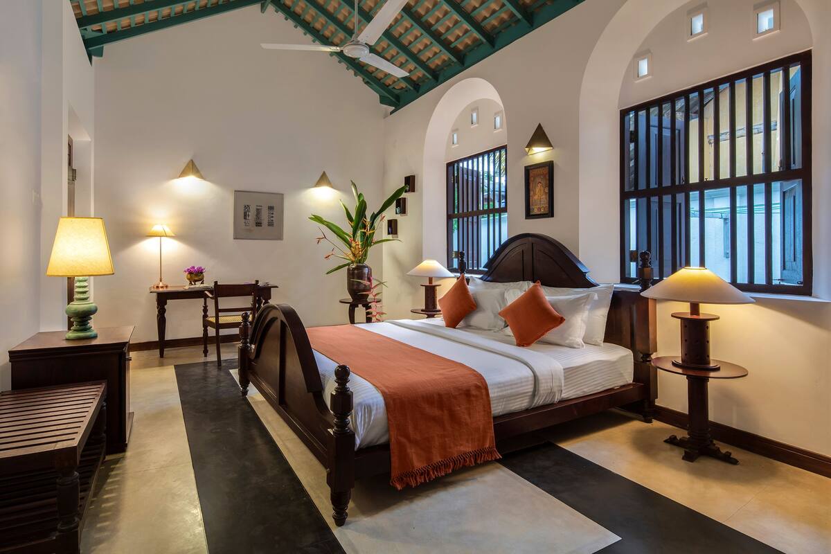 Habitación de hotel con cama, mesitas de noche, lámparas, una planta en maceta y vistas al exterior.