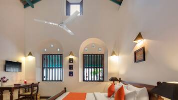 Habitación de hotel con cama, escritorio, silla, ventilador de techo y ventanas con rejas.