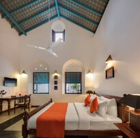 Habitación de hotel con cama, escritorio, silla, ventilador de techo y ventanas con rejas.