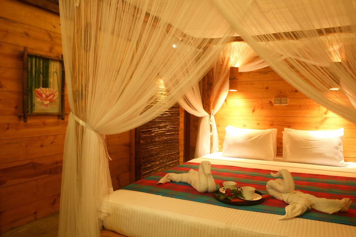 A wooden cabin room with a bed, white curtains, and a framed picture on the wall.