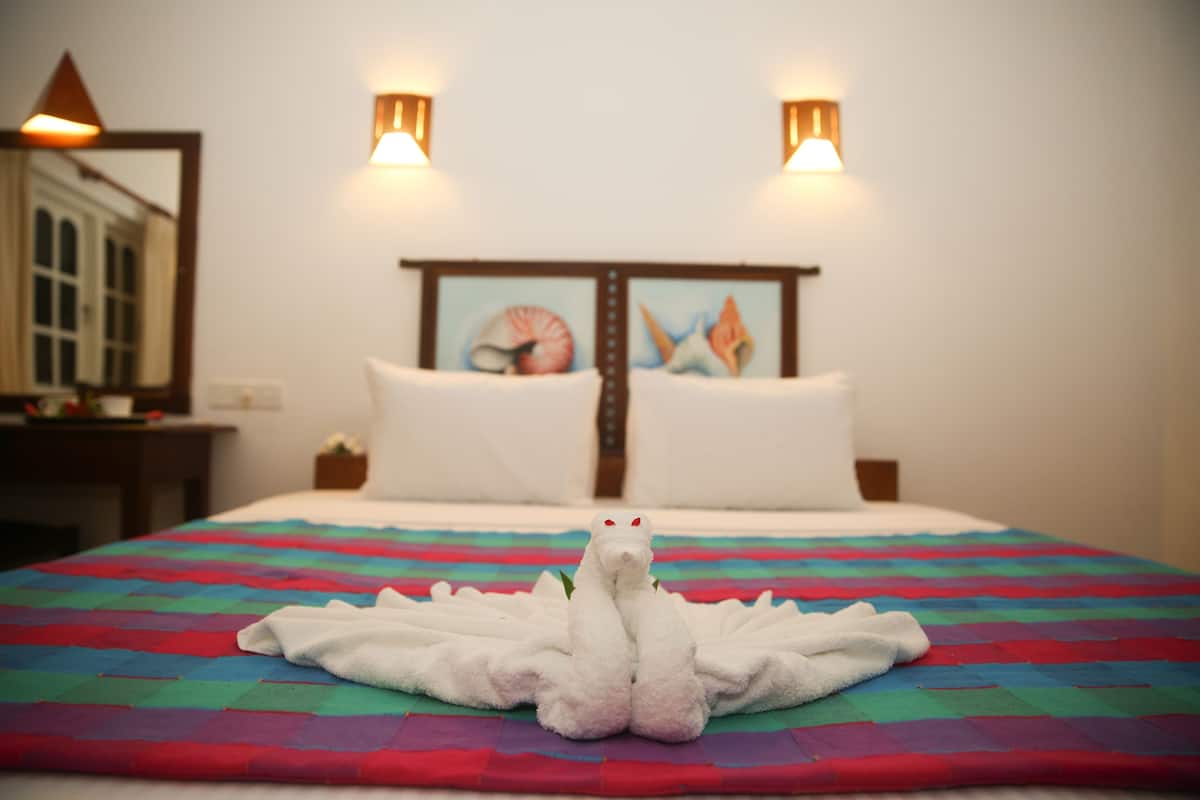 A bed with a colorful quilt, a white towel shaped like a swan, and a painting on the headboard.