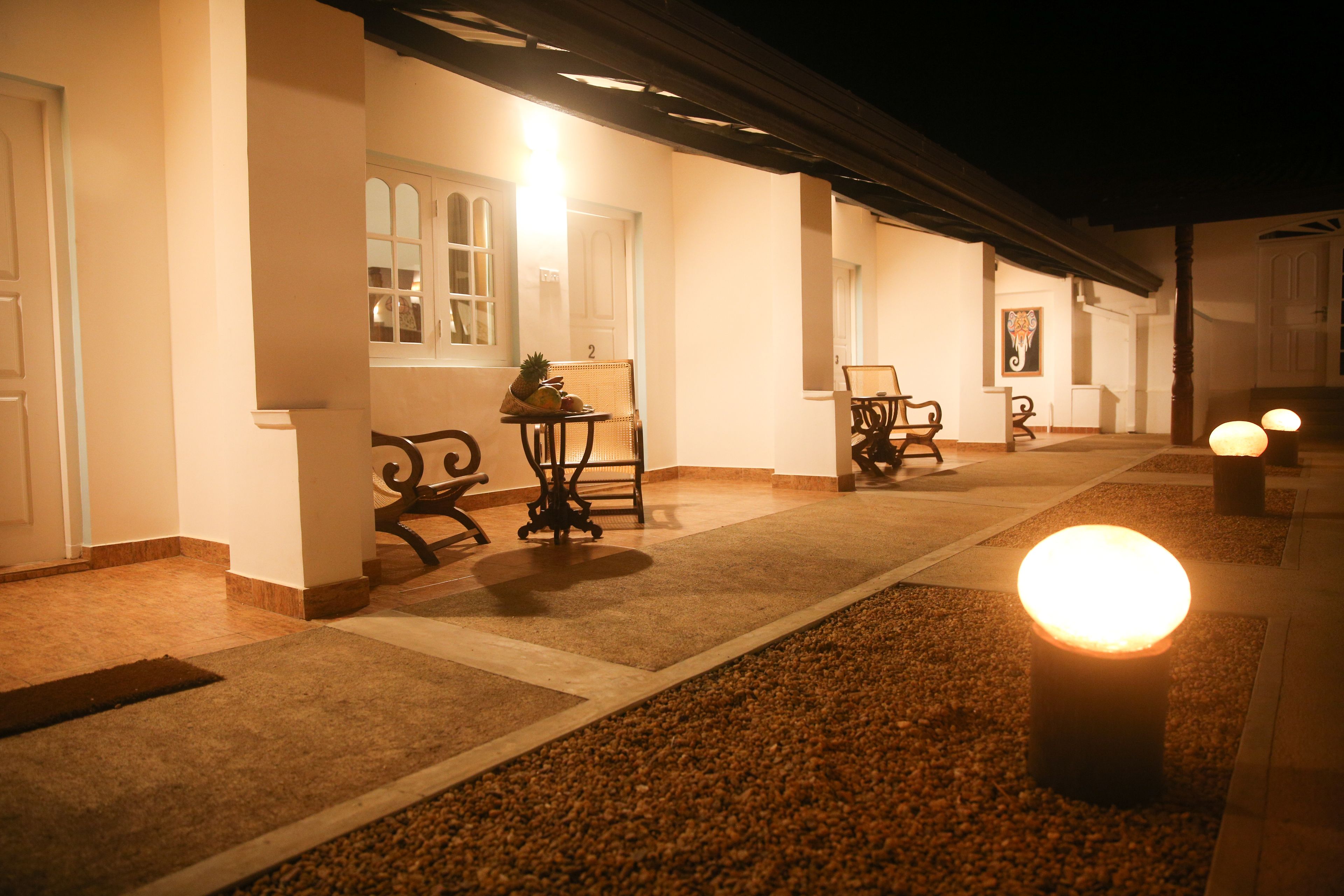 A corridor with a tiled floor, a bench, and a table with a pineapple on it. There are doors on the left and a wall with a picture on the right.