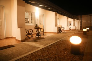 A corridor with a tiled floor, a bench, and a table with a pineapple on it. There are doors on the left and a wall with a picture on the right. - Thejan Beach Cabanas (Induruwa)