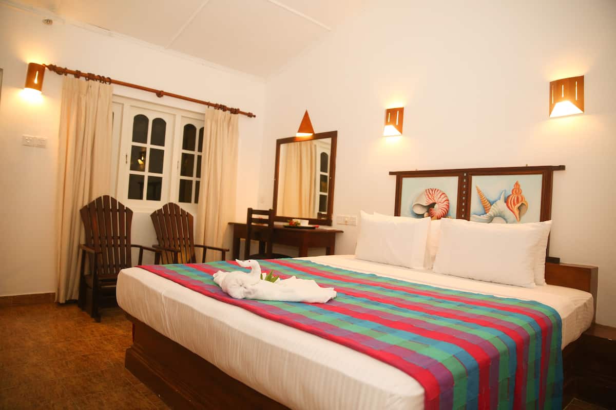 A hotel room with a large bed, a desk, a chair, and a window with curtains.