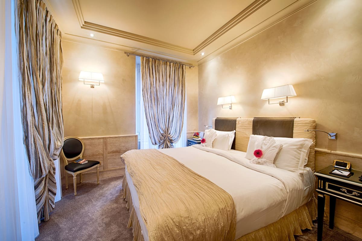 Una habitación de hotel con una cama grande, dos lámparas de noche, una mesita de noche y una silla.