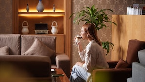A person sitting on a couch in a room with a wooden shelf containing decorative items and a potted plant. - Thousand Nights Hotel Amman (Amman)