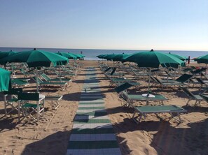 Een privéstrand, wit zand, ligstoelen aan het strand, parasols
