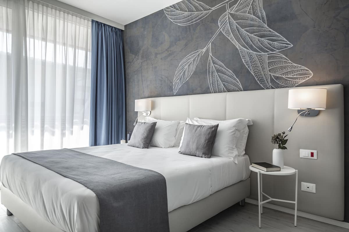 Et moderne hotelværelse med en stor seng, et natbord med lampe og et vægmaleri.