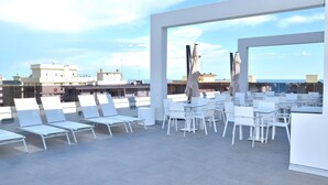 A rooftop terrace with white chairs and tables, offering a view of the cityscape and the sea. - Hotel Amburgo (San Michele al Tagliamento)