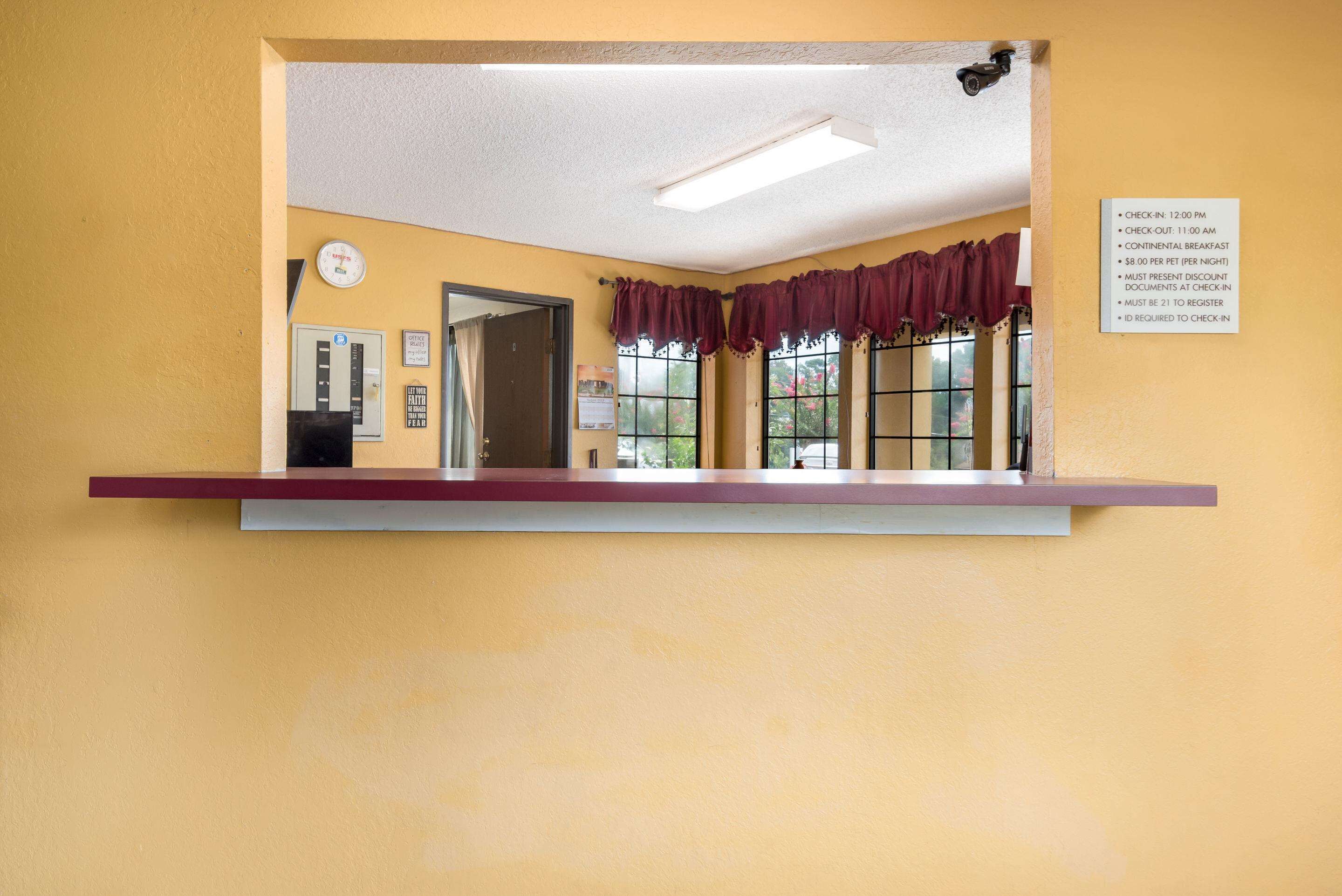 A reception area with a check-in counter, a clock, and a window with curtains.
