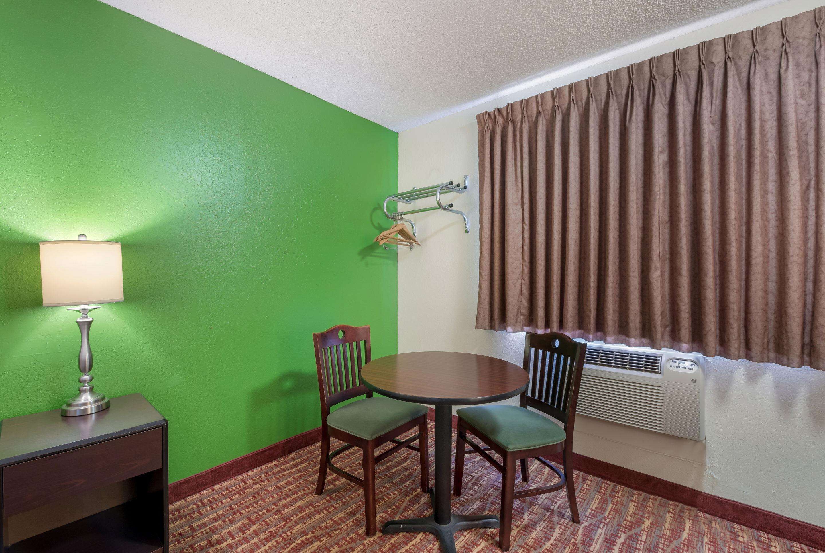 Una habitación con pared verde, una mesa redonda con cuatro sillas, una lámpara, un perchero y una ventana con cortinas.