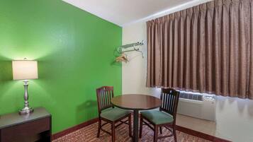 Una habitación con pared verde, una mesa redonda con cuatro sillas, una lámpara, un perchero y una ventana con cortinas.