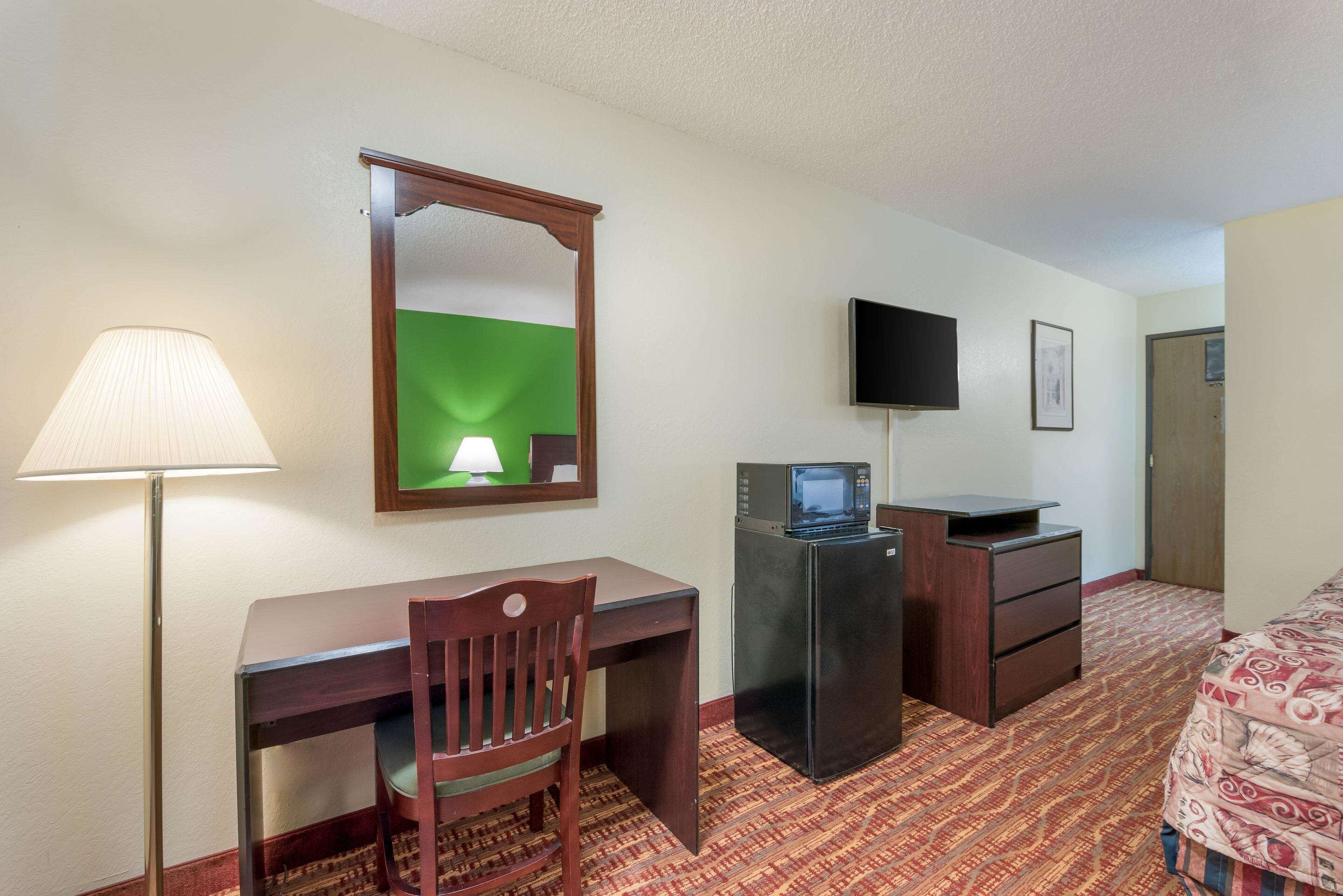 A hotel room with a desk, chair, lamp, television, and a bed with patterned bedding.
