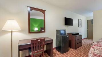 A hotel room with a desk, chair, lamp, television, and a bed with patterned bedding.