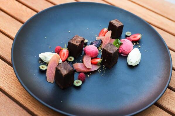 A dessert plate with various fruits and chocolate pieces on a dark plate. - Maison Bistro & Hotel (Budapest)