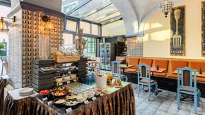 A breakfast buffet area with a variety of food items and a seating area with orange cushions. - Maison Bistro & Hotel (Budapest)