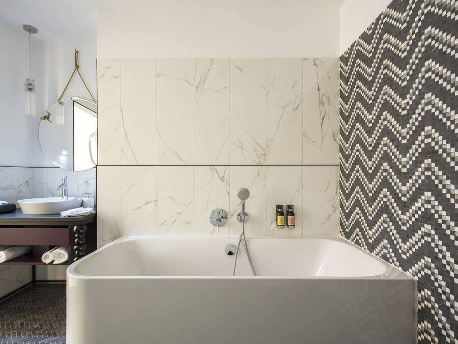 A modern bathroom with a freestanding bathtub, a vanity with a mirror, and a patterned tile wall.