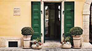 A building with a yellow facade, green doors, and potted plants at the entrance. - Maison Bistro & Hotel (Budapest)