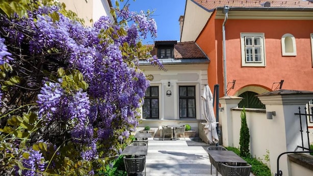 An outdoor patio area with tables and chairs, surrounded by purple wisteria flowers. - Maison Bistro & Hotel (Budapest)
