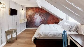 A bedroom with a wooden floor, a bed with white bedding, a TV mounted on the wall, and a decorative mural on the wall.