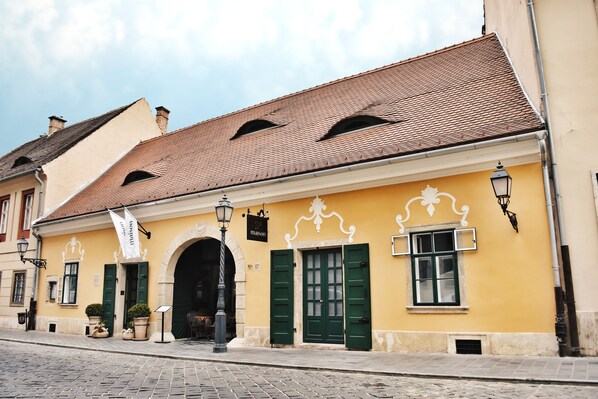 Um edifício amarelo com persianas verdes, telhado de telhas e rua de calçada.