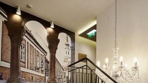A staircase with a black railing and a chandelier, leading to a room with a patterned wall and a view of a building facade. - Maison Bistro & Hotel (Budapest)