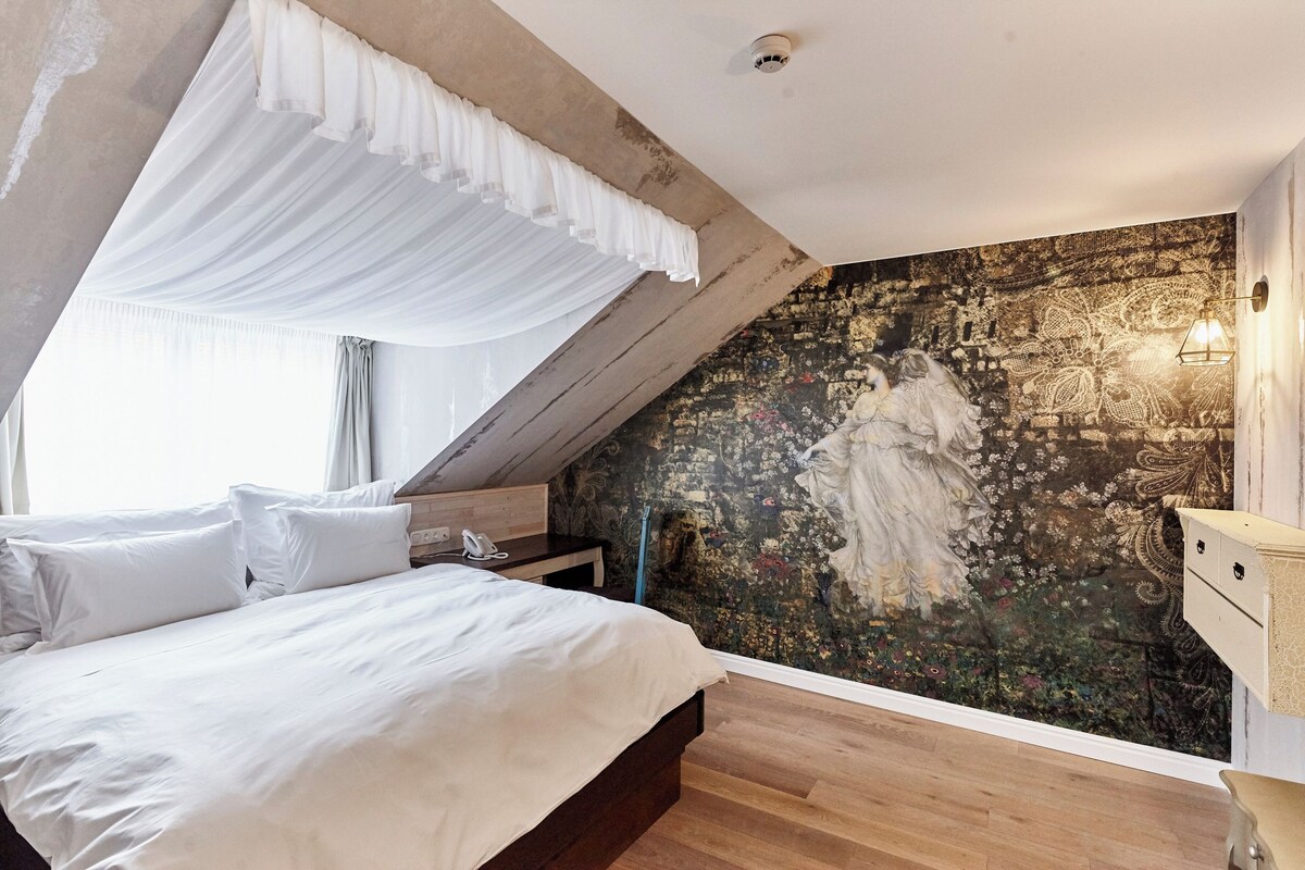 Une chambre à coucher comprenant un lit, une table de chevet, une fresque murale et un ventilateur de plafond.
