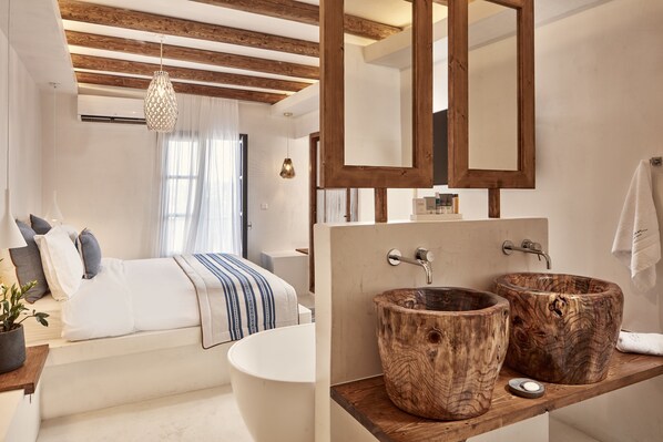 A modern bedroom with a large bed, a wooden ceiling, and a large mirror above the bathroom sink. - Parian Boutique Hotel (Paros)