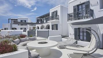 Relax in a serene outdoor space with a round table and comfortable seating, surrounded by lush greenery and a balcony with a railing.