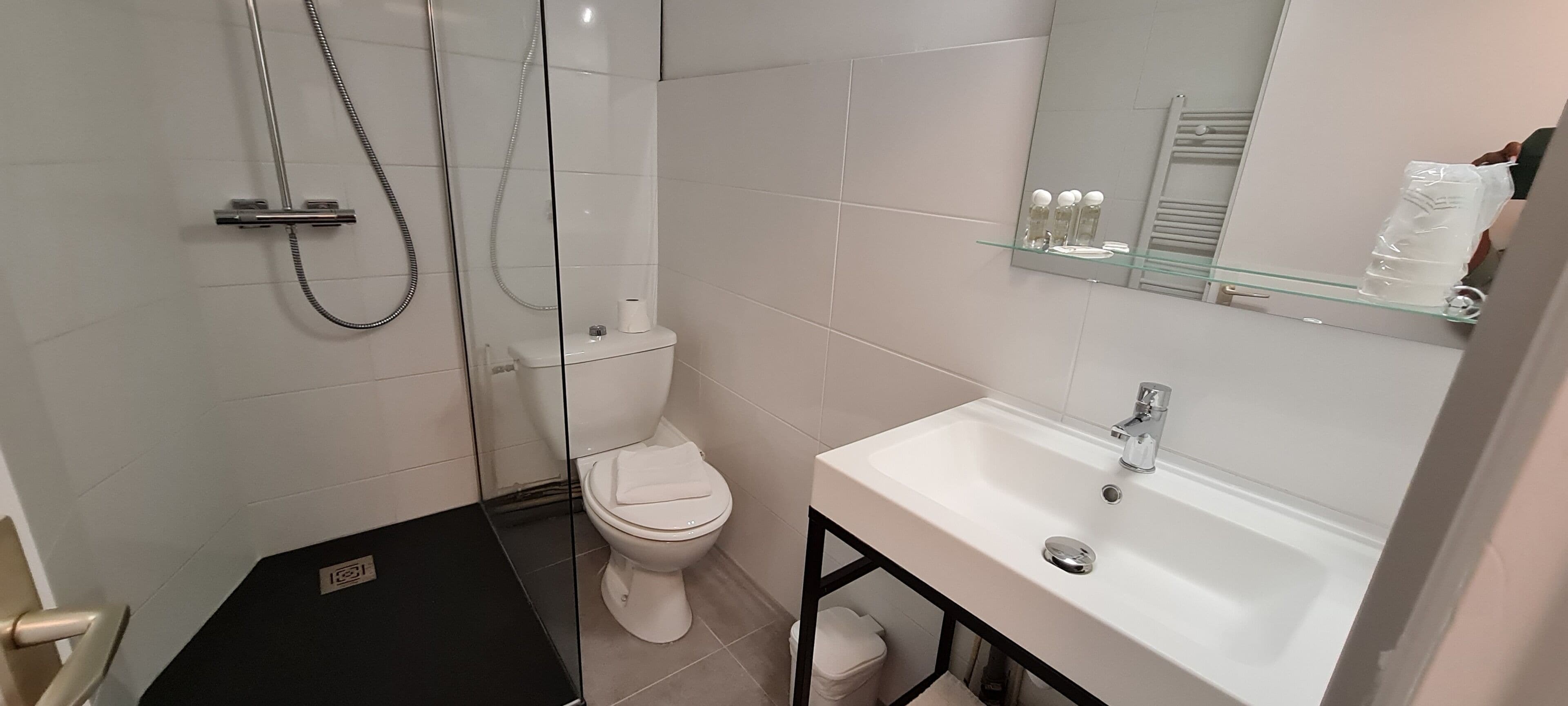 A modern bathroom with a glass-enclosed shower, a white toilet, and a white sink with a mirror above it.