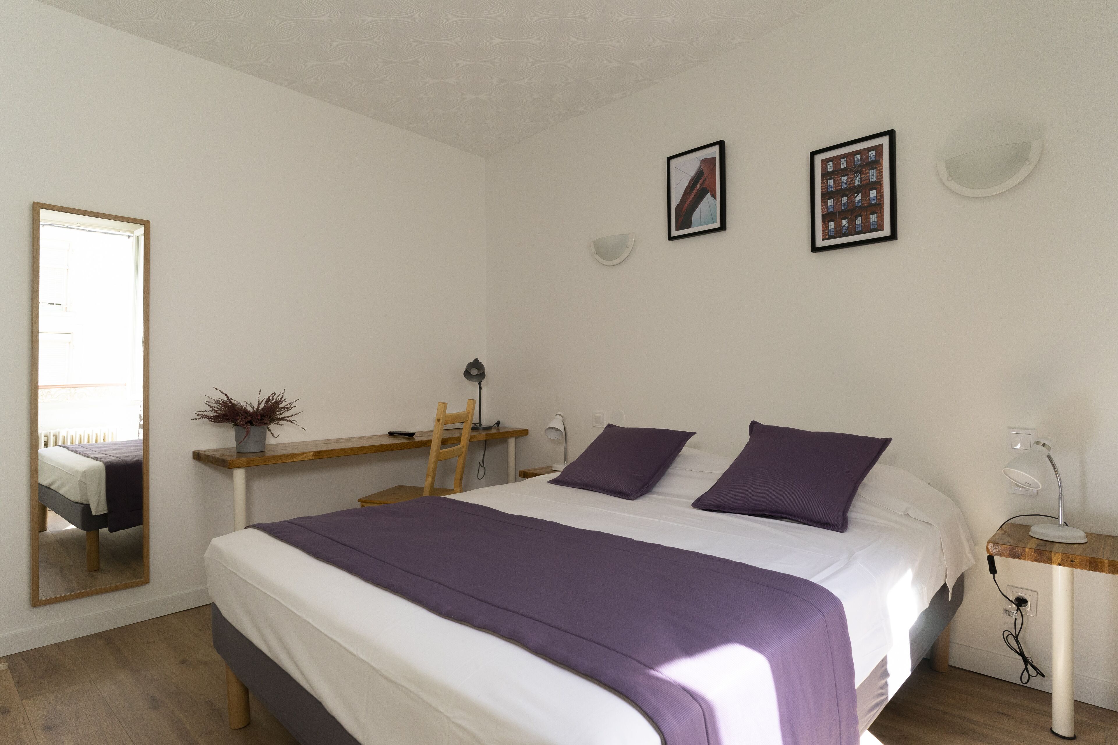 Une chambre à coucher comprenant un lit, un bureau, une chaise, un miroir et une étagère fixée au mur.