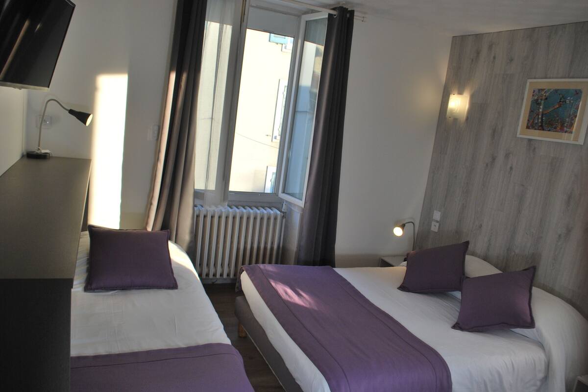 Habitación de hotel con dos camas, un radiador, una ventana con cortinas, una lámpara de pared y un cuadro.