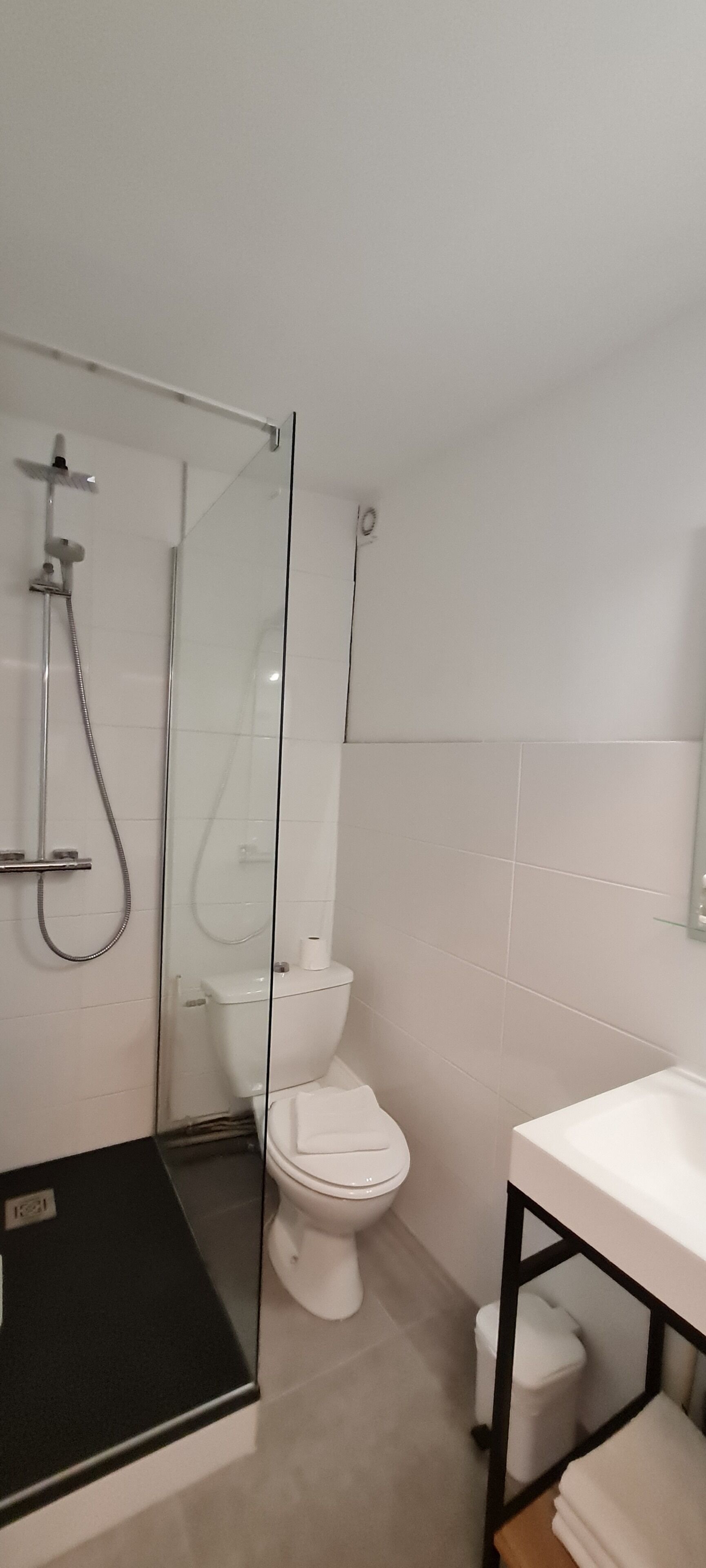 A modern bathroom with a glass-enclosed shower, a white toilet, and a sink with a black countertop.
