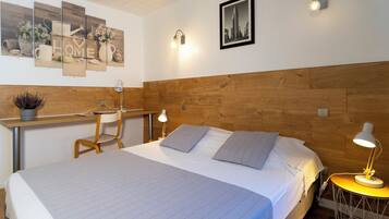A bedroom with a wooden headboard, a bed with grey bedding, two bedside lamps, a desk with a chair, and a wall art piece with the word "HOME".