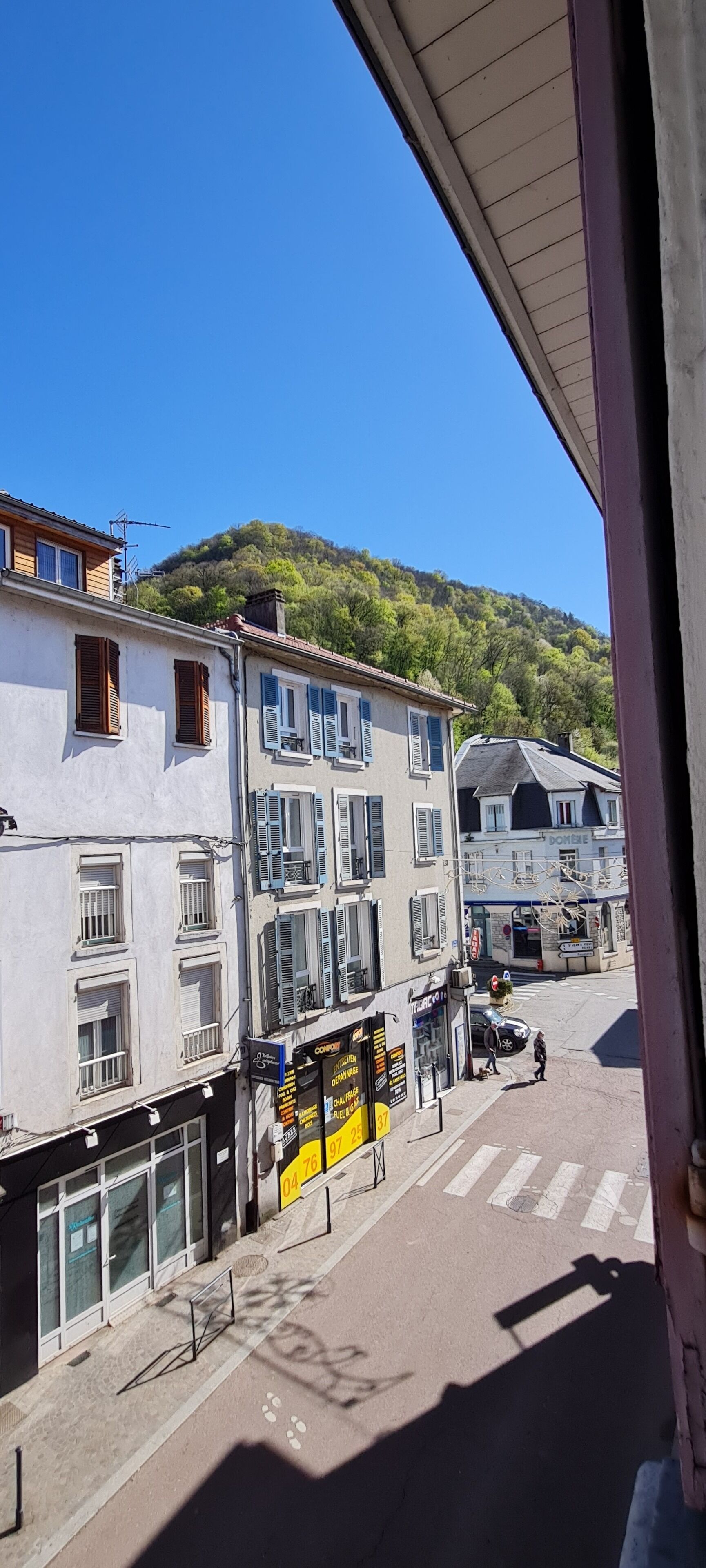 A street view with buildings, a clear sky, and a hilly background.