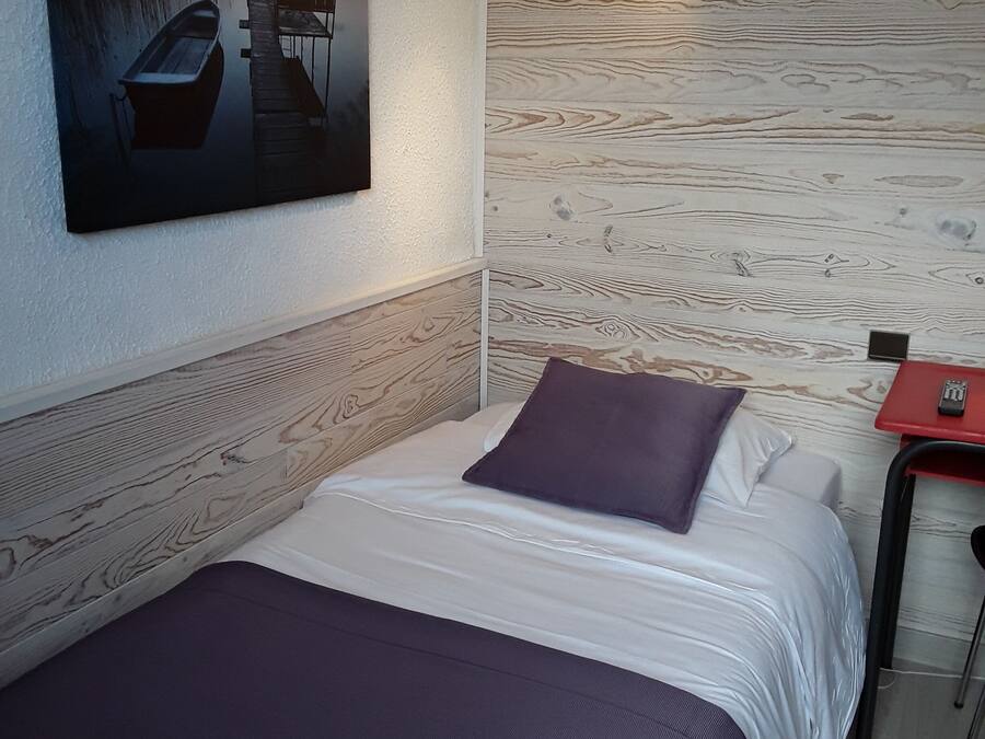 Un letto rifatto con cura, una coperta e un cuscino viola, un quadro raffigurante una barca e una parete con decorazioni in legno.