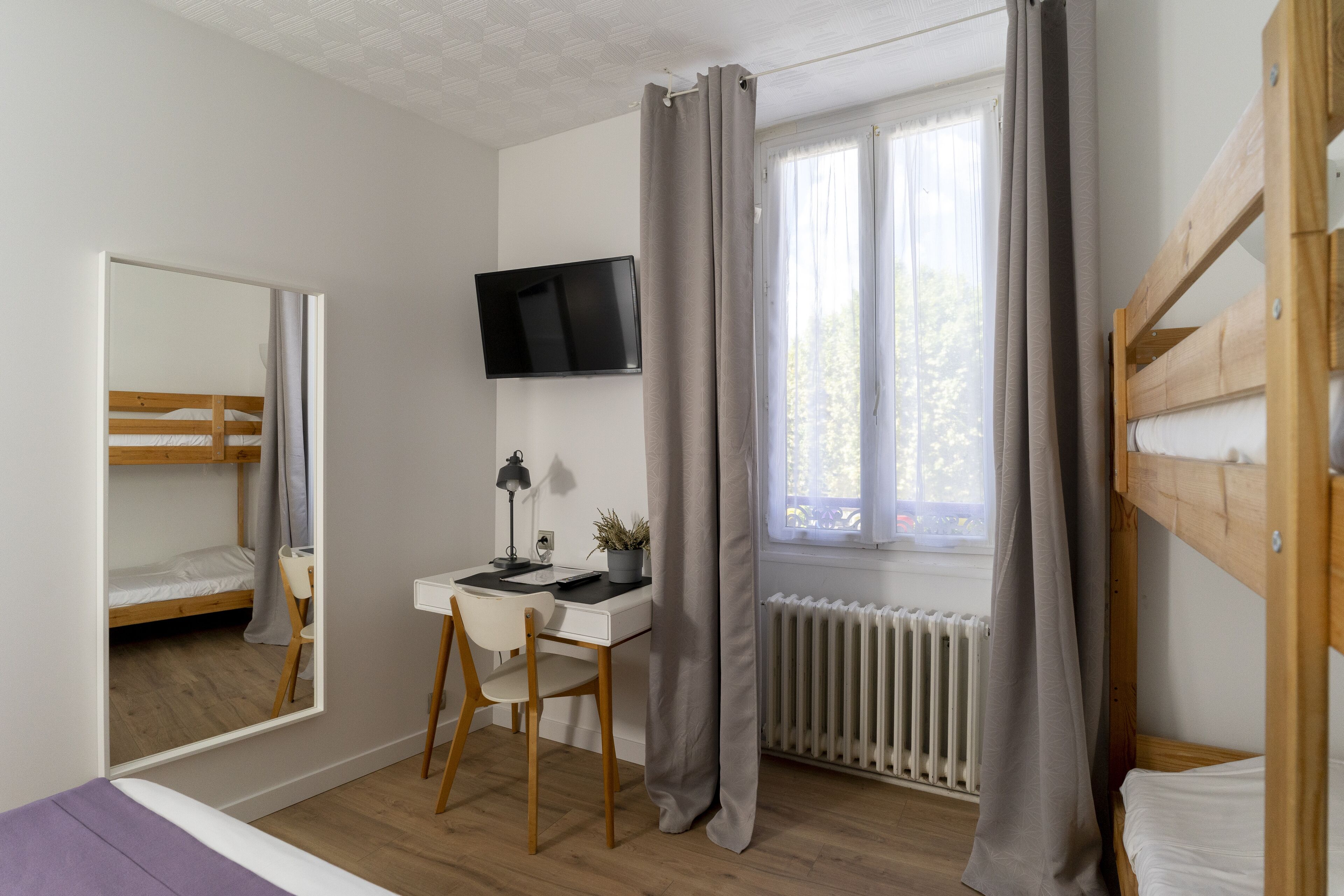 Ein Schlafzimmer mit Etagenbett, Schreibtisch mit Stuhl, Wandfernseher und einem Fenster mit Vorhängen.