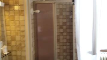 Une salle de bain avec un mur carrelé, une douche, un lavabo et des toilettes.