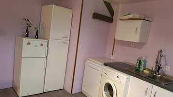 Een kleine keuken met een koelkast, wasmachine en een spoelbak met kraan.
